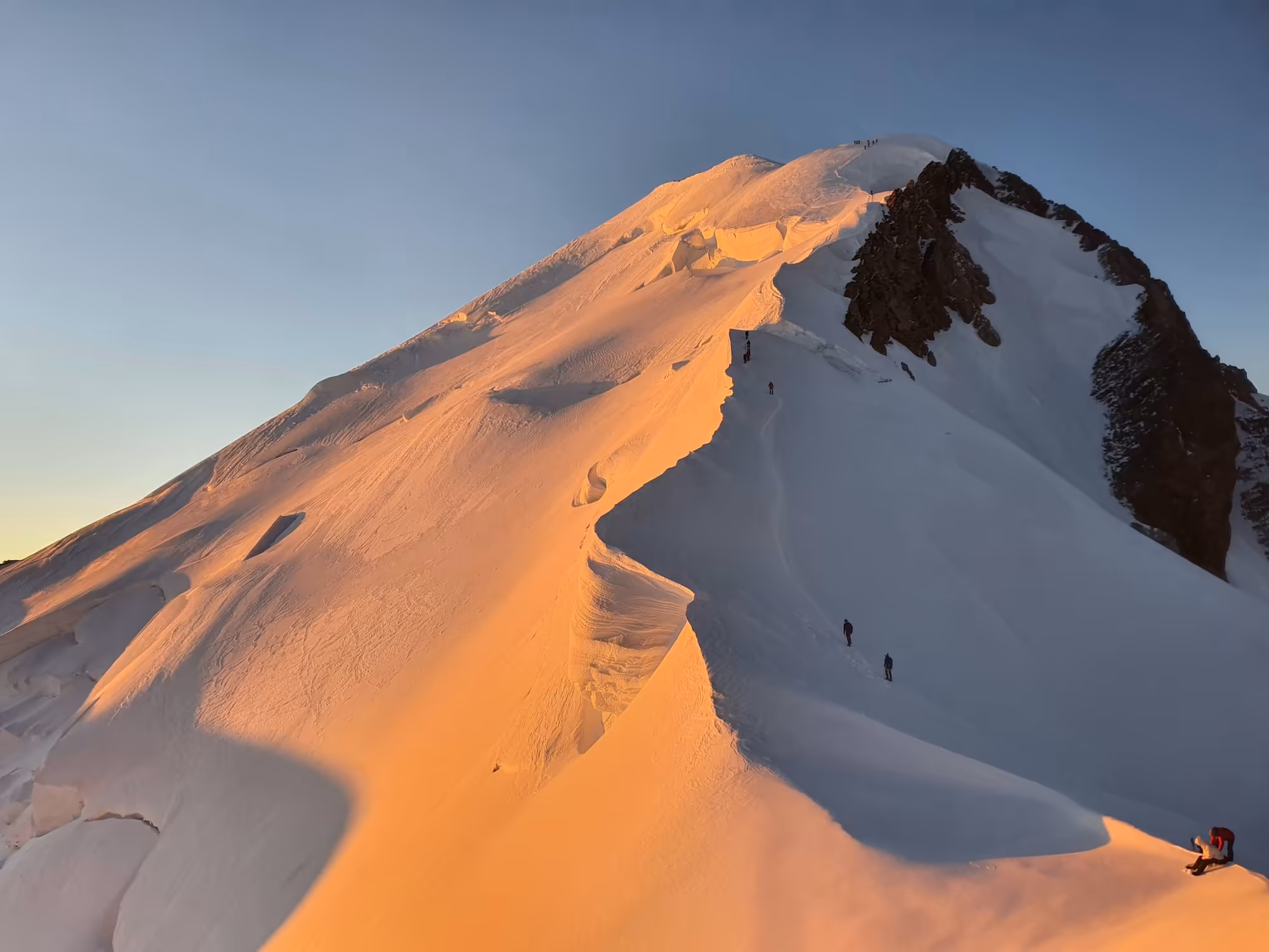 Climbers on a snowy ridge near the top of Mont Blanc at sunrise.
